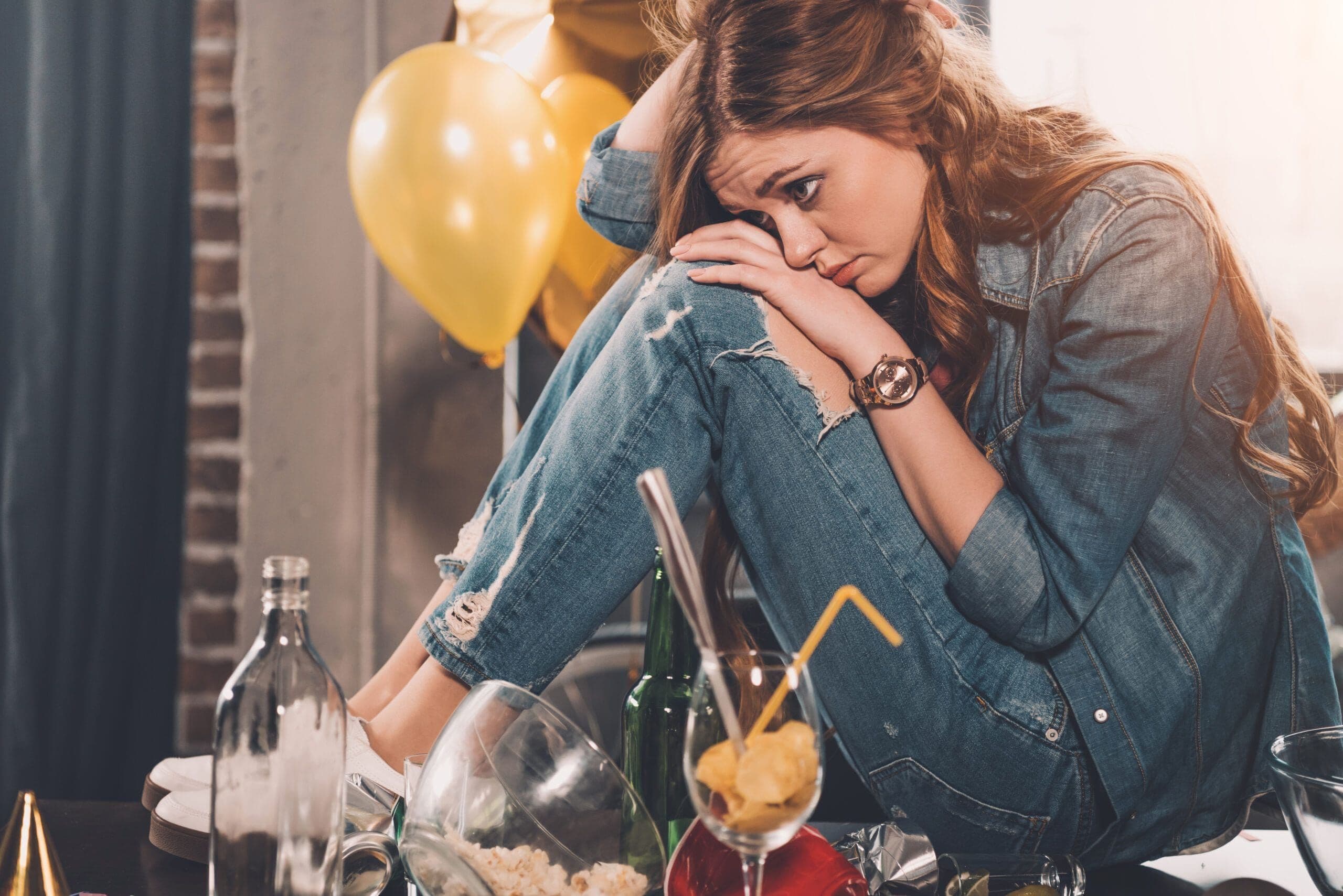 Woman feeling emotional after drinking after Dry January, surrounded by empty glasses and bottles
