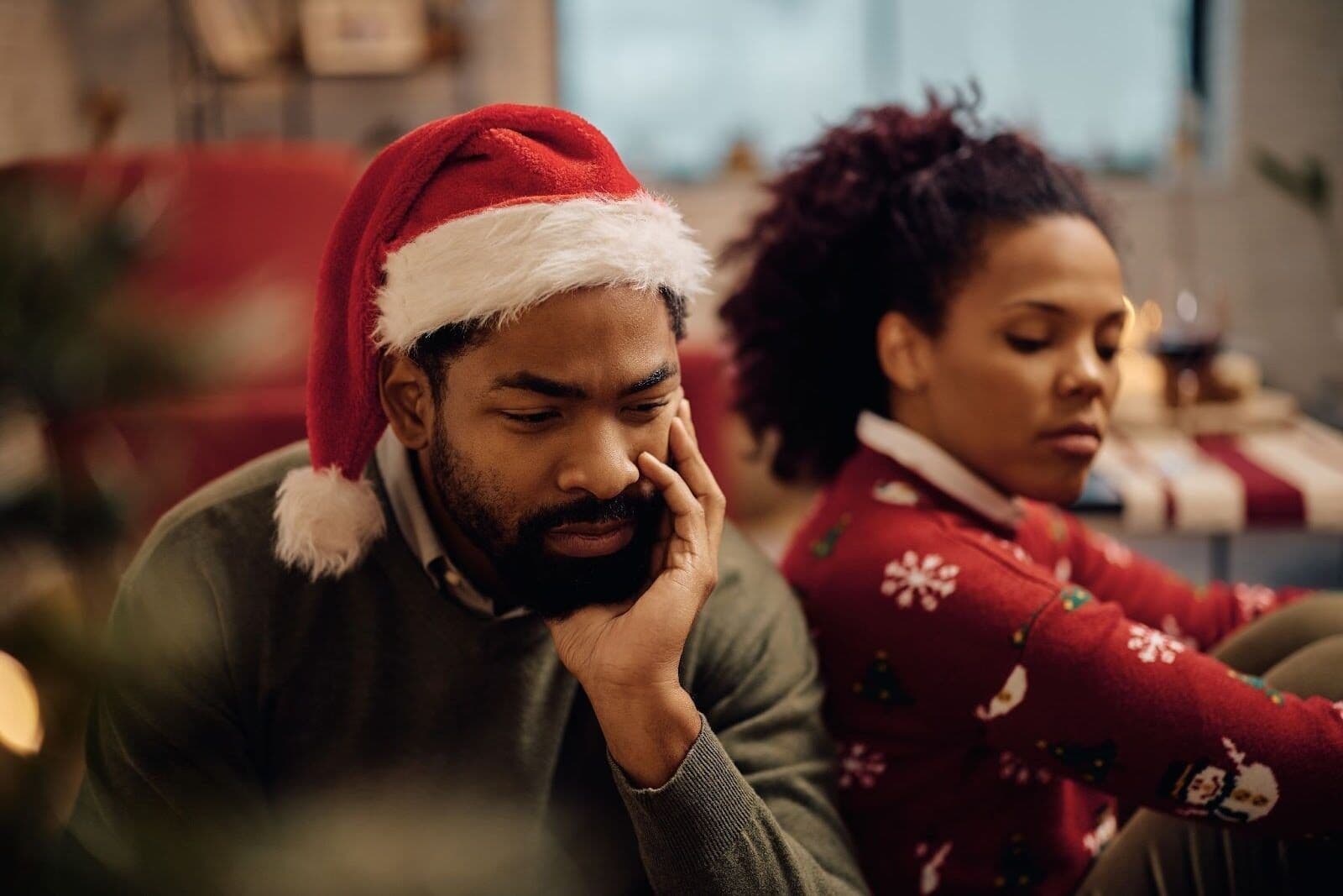 A person experiencing grief at Christmas, sitting quietly in a holiday setting with a partner nearby, reflecting the emotional weight the season can bring.