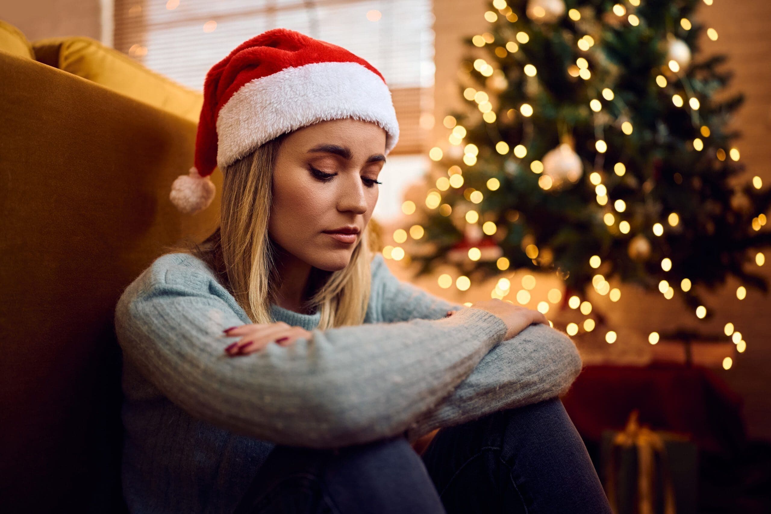 A woman sitting alone in holiday lights wearing a Santa hat, reflecting grief at Christmas