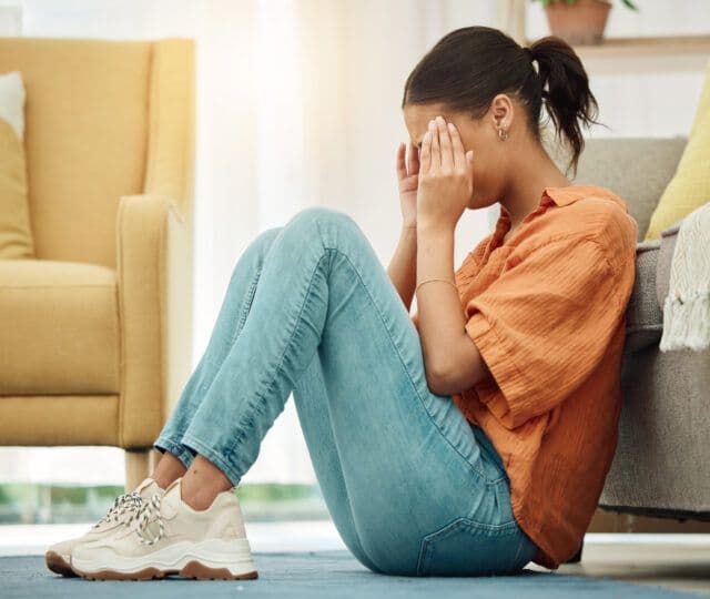 Woman sitting on the floor with her head in her hands, showing stress linked to attachment issues and emotional struggles.