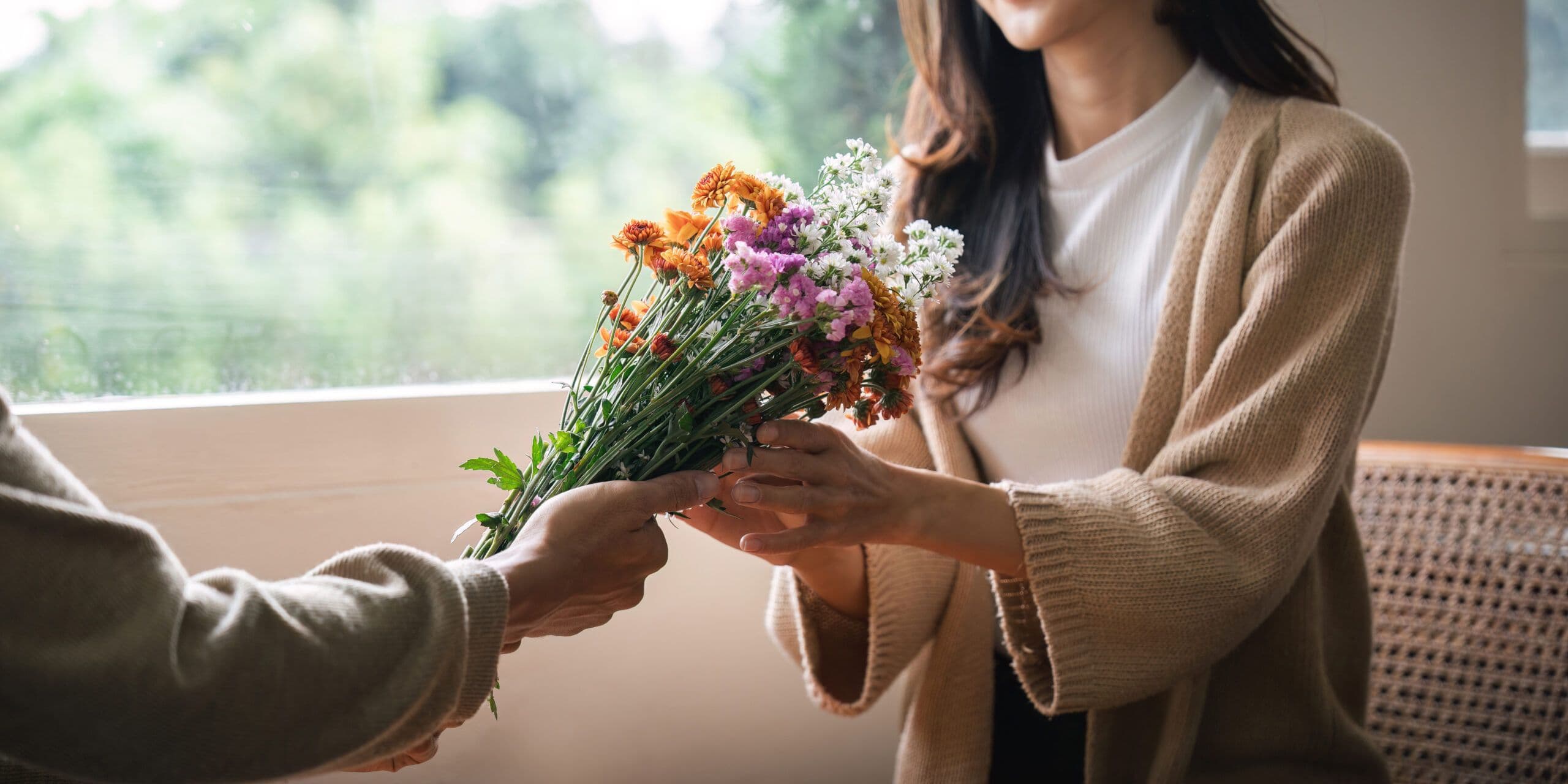 Romantic young asian couple embracing with holding flowers and smiling in living room at home. fall in love. Valentine concept