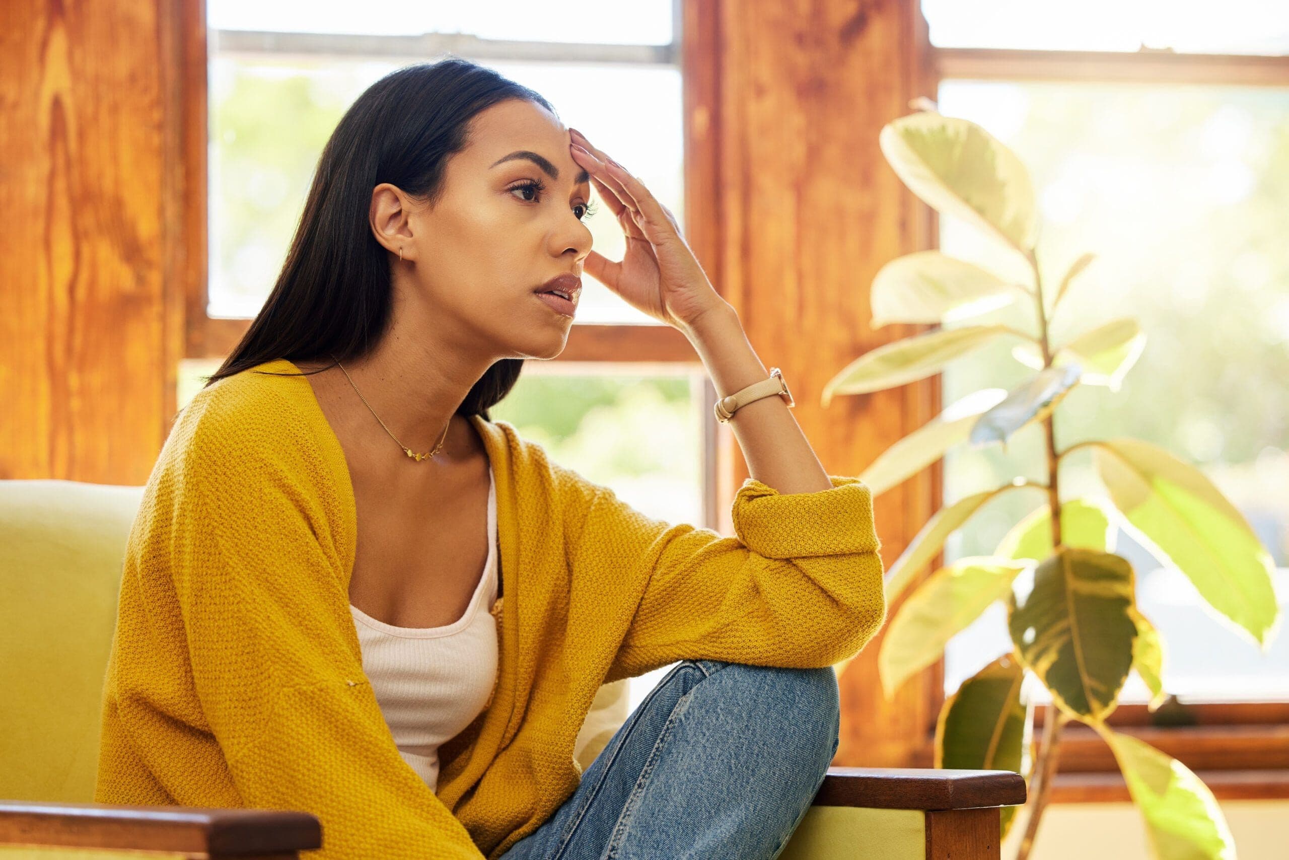 Woman sitting thoughtfully by a window, feeling the pressure of perfectionism and self-criticism.