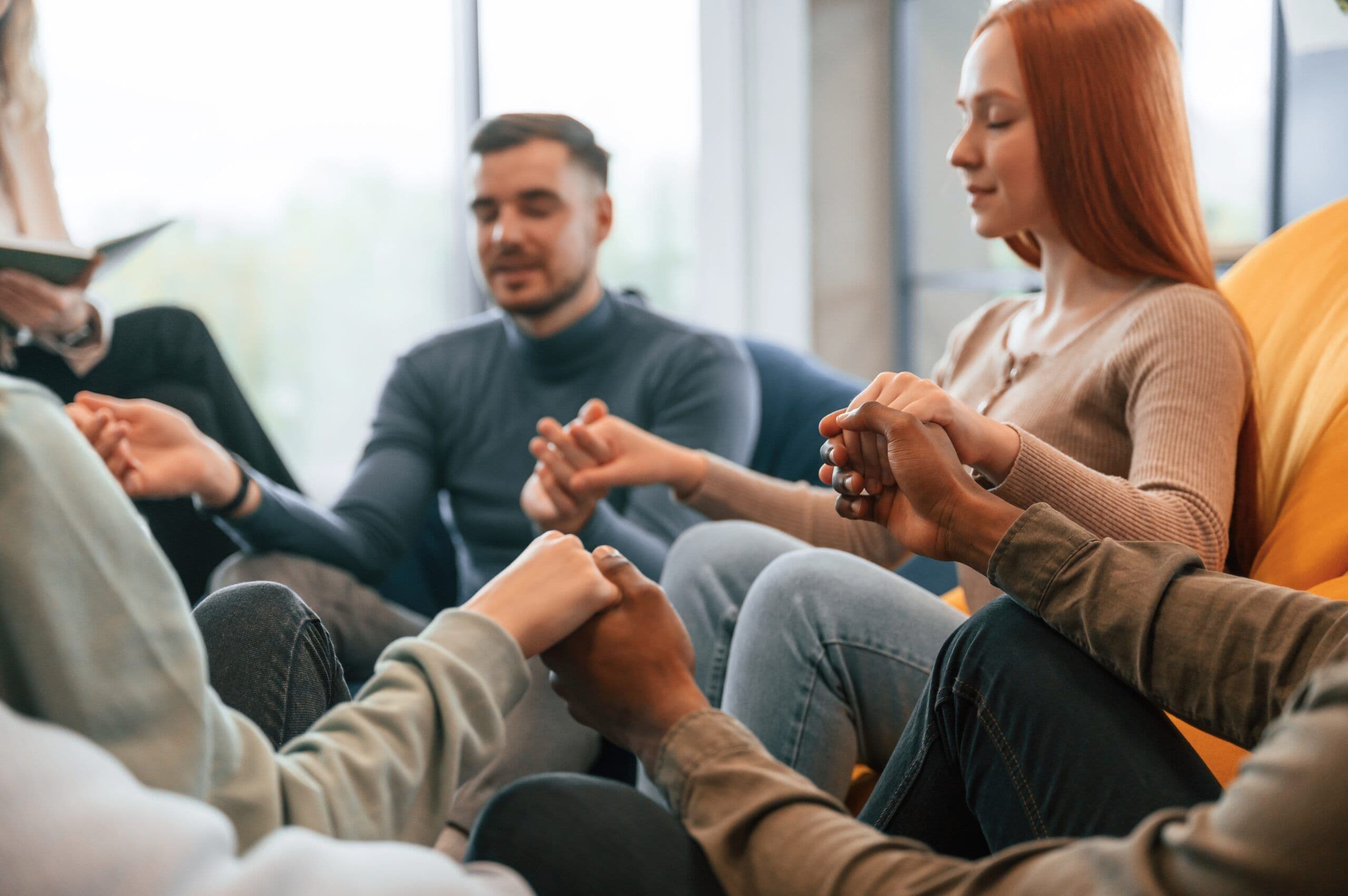 Sitting and holding each other by hands. Group of people are having therapy meeting together
